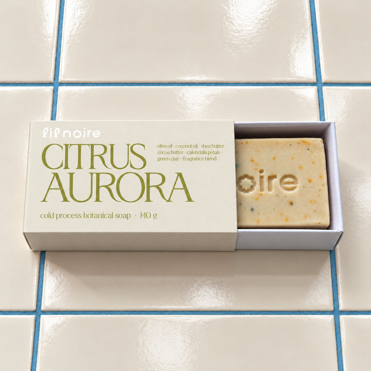 Citrus Aurora 140 g botanik sabun, açık çekmeceli kutu; krem fayans ve mavi derz üzerinde